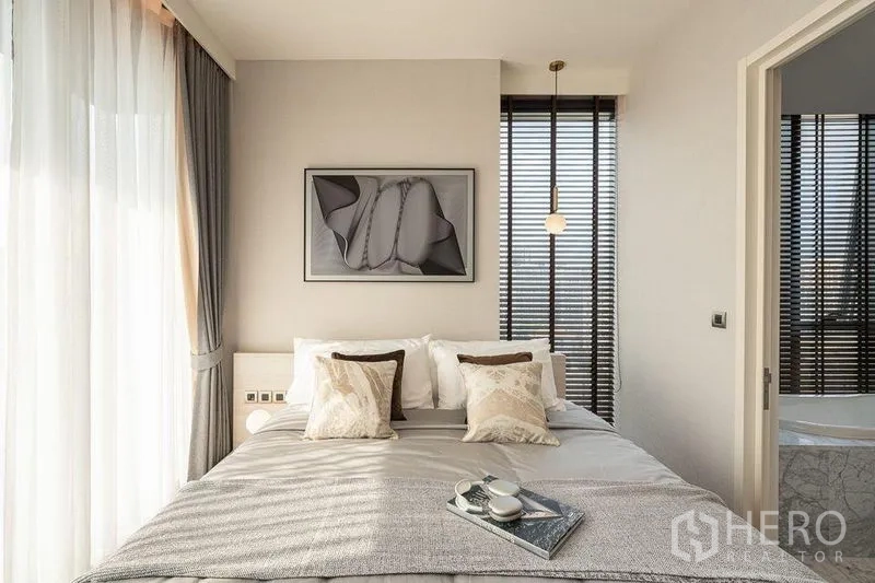 Condominium for rent in Watthana, Bangkok - Sunlit master bedroom with corner windows, wall art, and door to a spa-style ensuite.