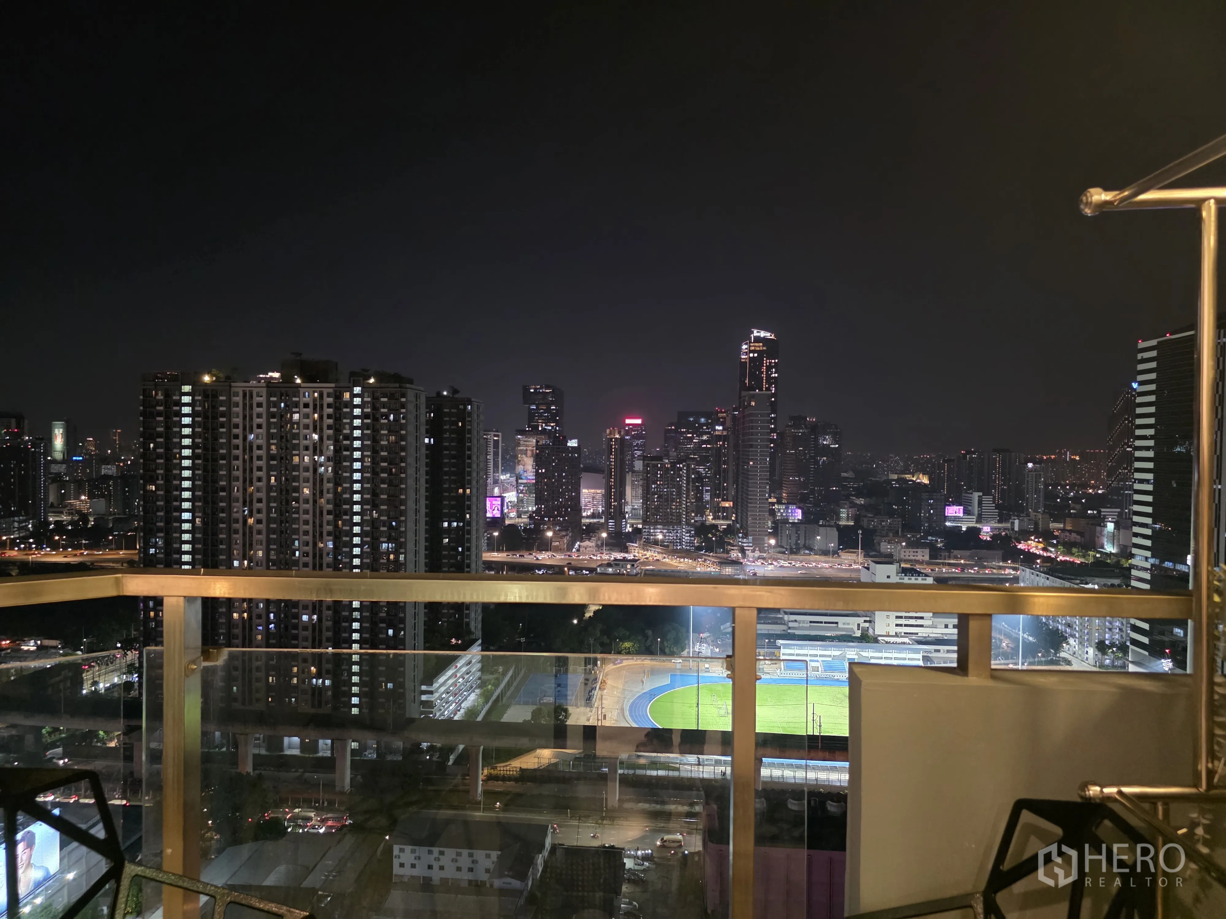 公寓 for rent in Bang Kapi, Bangkok - 高楼阳台夜景，可见城市天际线与亮起的运动场。