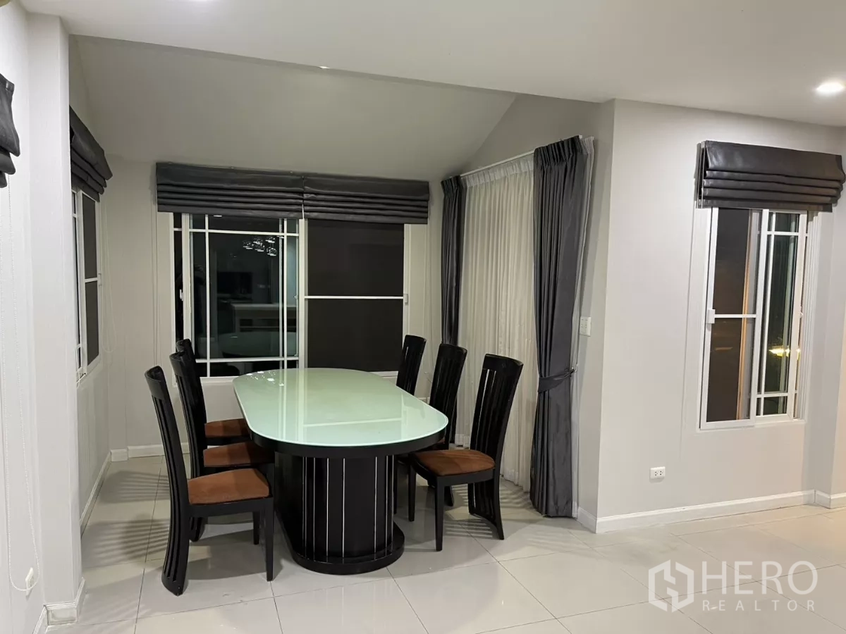 Detached House for rent in Bang Kapi, Bangkok - Dining corner with glass-top table and six chairs beside large windows and curtains.