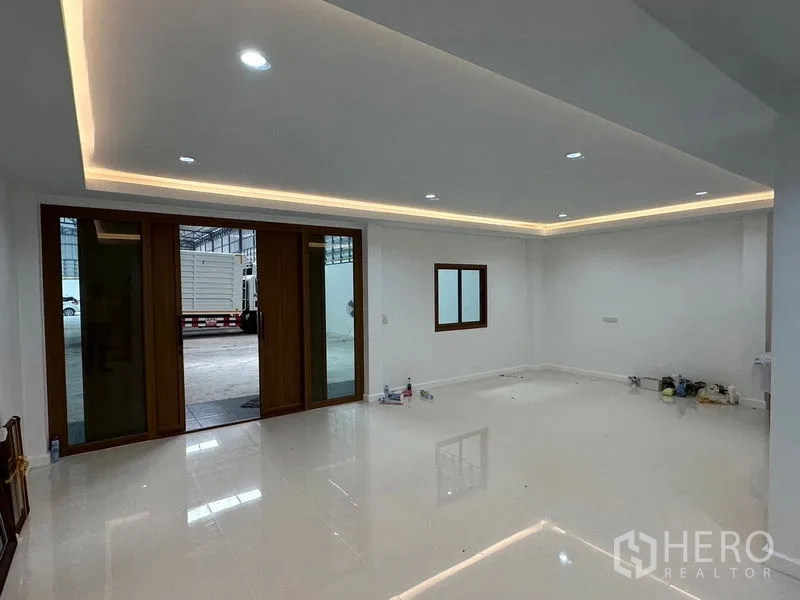 Warehouse for rent in Lam Luk Ka, Pathum Thani - Bright ground-floor office or reception with glossy white tiles, recessed LED strip lighting and glass doors to the warehouse.