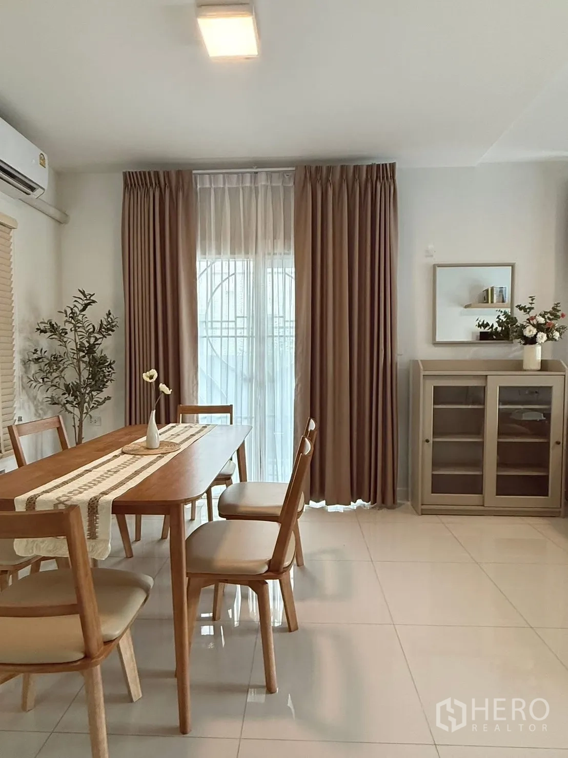 Detached House for rent in Bang Phli, Samut Prakan - Dining area with wooden table and chairs beside full-height curtains and a display cabinet.