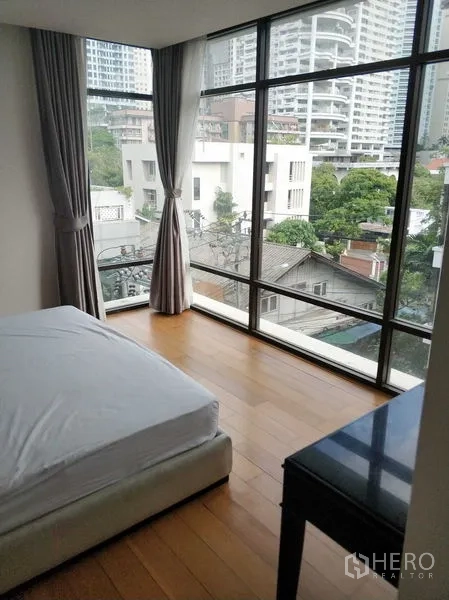Condominium for rent in Khlong Toei, Bangkok - Corner bedroom with floor-to-ceiling windows offering a city view over Khlong Toei.