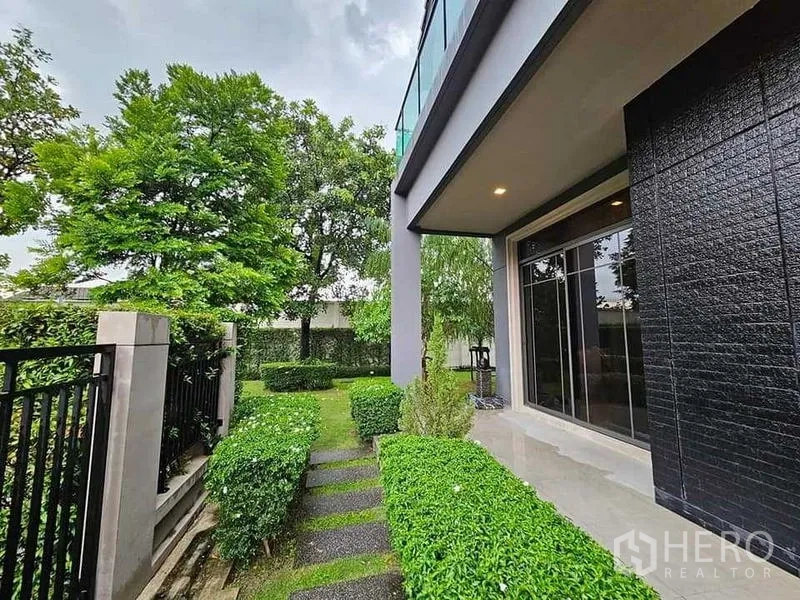 Detached House for sale in Bang Kruai, Nonthaburi - Pathway along the house with manicured hedges, sliding doors and a glass-railed balcony above.
