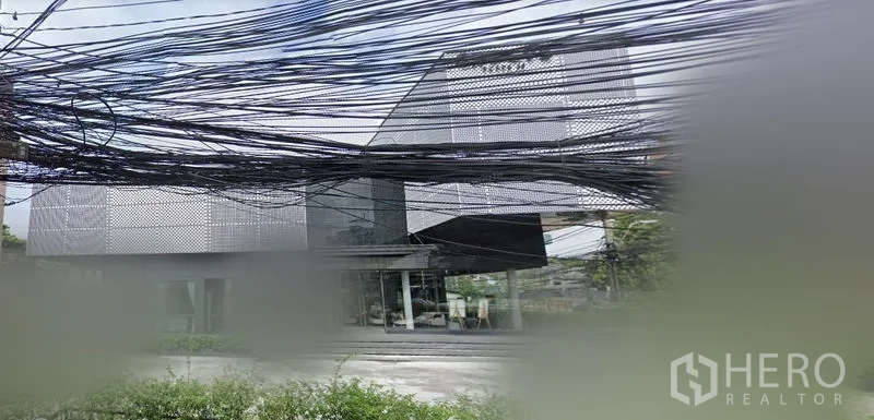 พื้นที่ขายปลีก ให้เช่าในHuai Khwang, Bangkok - อาคารค้าปลีกสไตล์โมเดิร์นในห้วยขวาง ฟาซาดโลหะเจาะรู หน้าร้านกระจกเต็มบาน ลานจอดรถด้านหน้า และสายสื่อสารเหนือศีรษะ