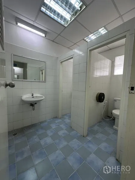 Factory for rent in Nonthaburi - Clean tiled restroom with toilets, sink and fluorescent lighting.