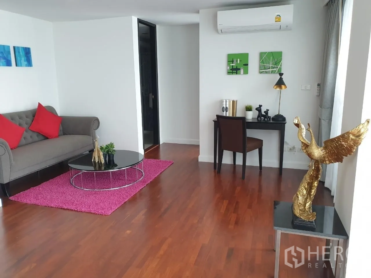 Apartment for rent in Bang Rak, Bangkok - Secondary lounge with tufted sofa, pink rug and compact work desk by windows.