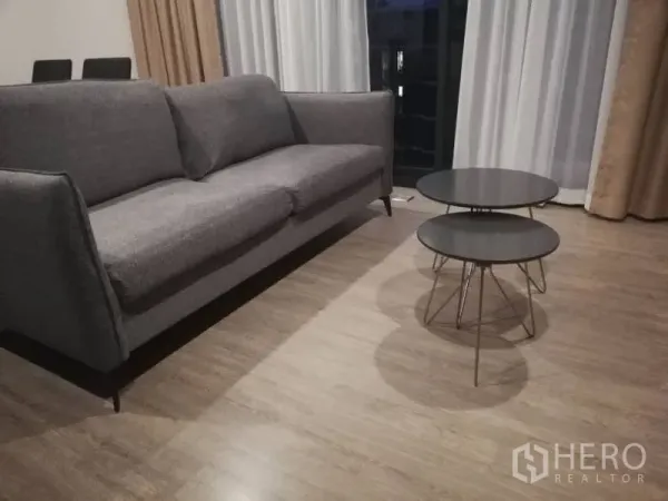 公寓 出租在Watthana, Bangkok - 灰色布艺沙发特写，旁有两张圆形套叠茶几，木地板与阳台窗前采光充足。