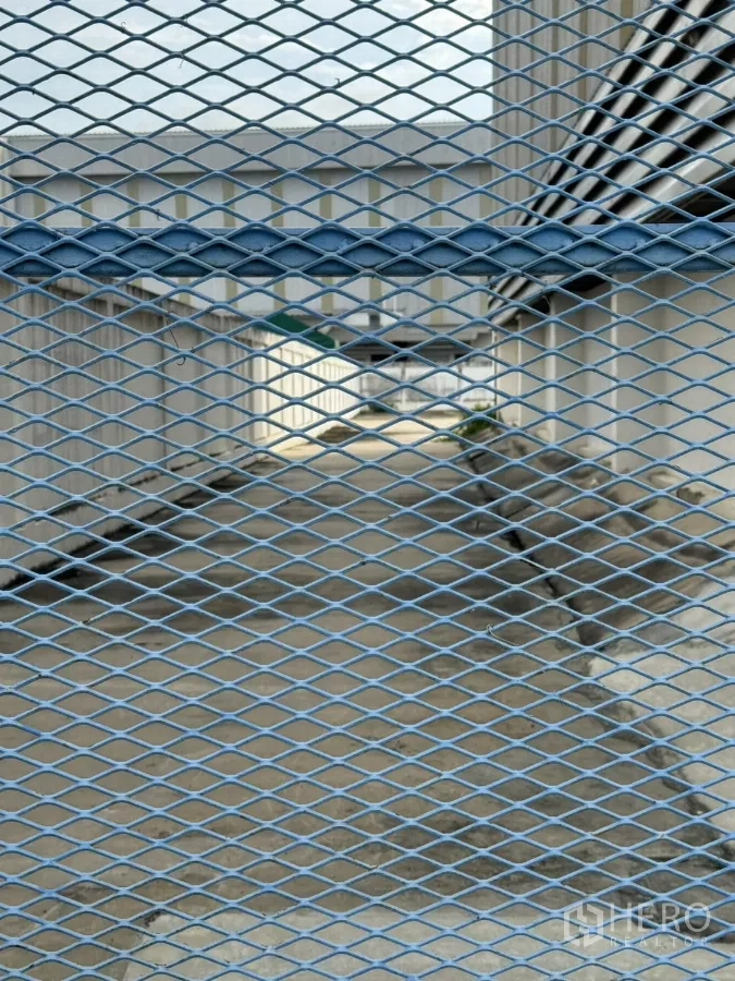Factory for rent or sale in Bang Phli, Samut Prakan - View through metal mesh to side service passage between buildings.