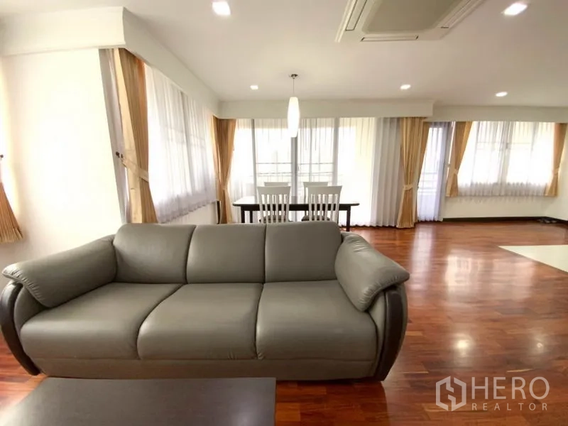 公寓 出租在Watthana, Bangkok - 以沙发为中心的客厅，环绕落地窗，后方为餐桌，配吊顶空调。