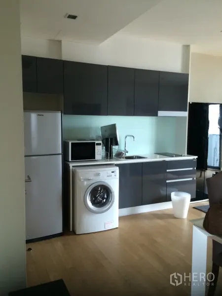 Condominium for rent in Watthana, Bangkok - Modern built-in kitchen with glossy grey cabinets, fridge, microwave and in-unit washer in an Ekkamai condo.