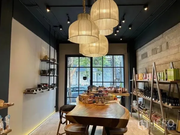 零售空间 出租在Bang Rak, Bangkok - 精品店视角，大型吊灯、原木中岛吧台、吧凳与临街落地窗。