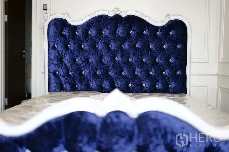 Condominium for rent in Khlong Toei, Bangkok - Close view of deep blue tufted headboard with crystal buttons and white trim.