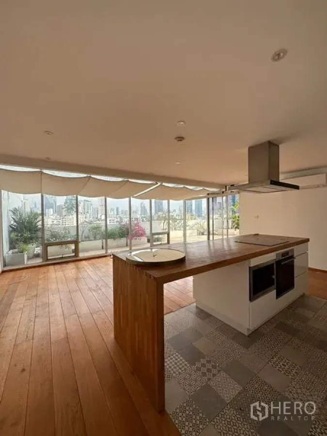 Condominium for rent in Khlong Toei, Bangkok - Kitchen island in open living area beside large windows and terrace with city view.