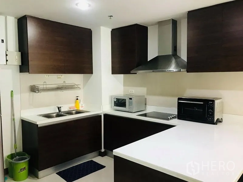 公寓 出租在Pathum Wan, Bangkok - L型厨房，深色橱柜、白色台面、双水槽与家电。