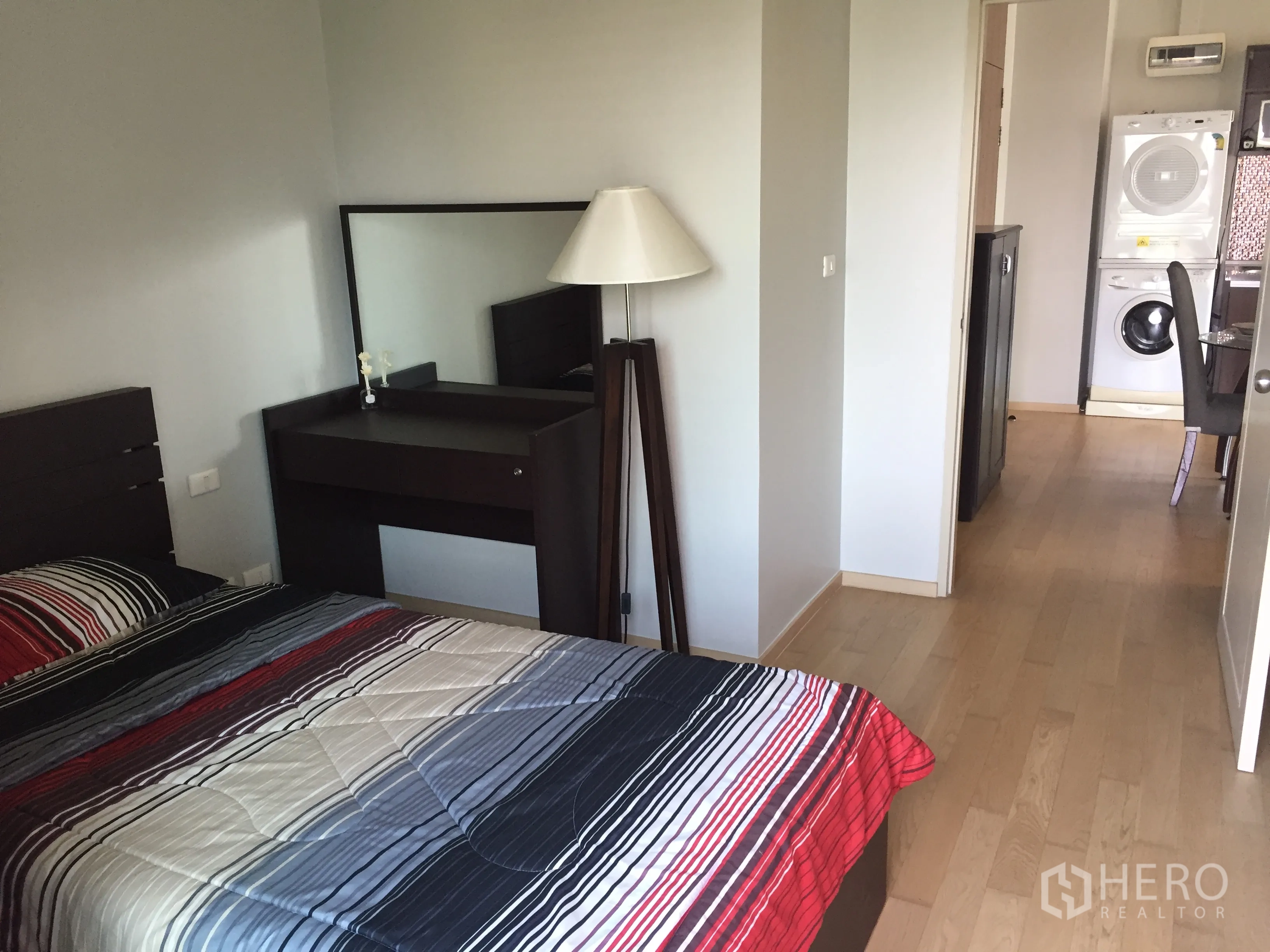 Condominium for rent in Watthana, Bangkok - Second bedroom with striped bedding, dressing table and light wood floors looking toward the kitchen and laundry unit.
