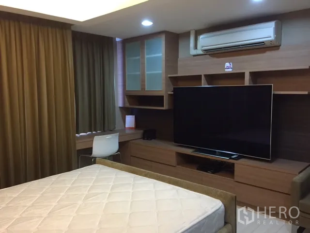 Condominium for rent or sale in Khlong Toei, Bangkok - Master bedroom featuring a large TV, work desk, wood cabinetry and air conditioner.