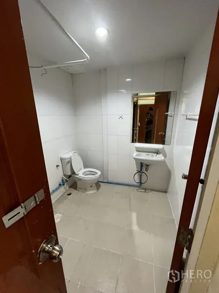 Shophouse for rent in Khlong Toei, Bangkok - Bathroom with white wall tiles, toilet, sink, and mirror under ceiling lighting.