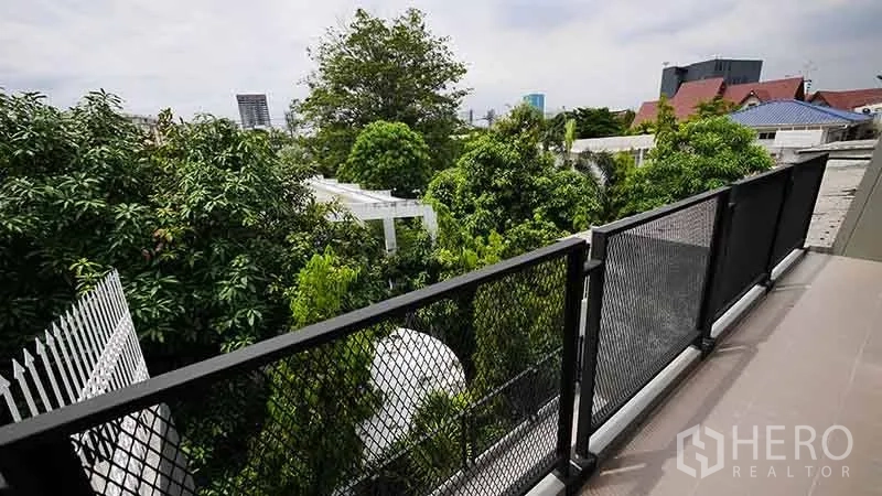 Townhouse for rent in Watthana, Bangkok - Balcony with mesh railing overlooking mature trees and distant skyline.