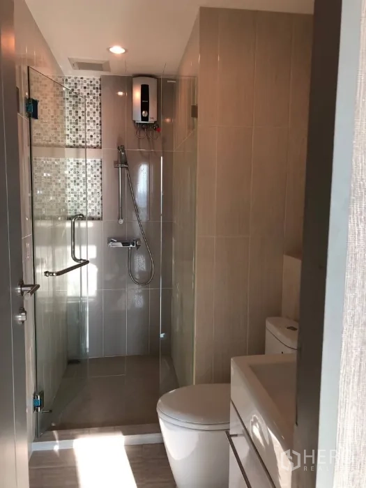 Condominium for rent or sale in Huai Khwang, Bangkok - Modern bathroom with a glass-enclosed shower, handheld spray and water heater.