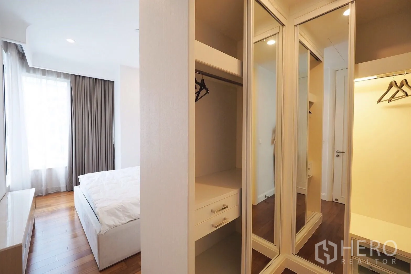Condominium for rent in Pathum Wan, Bangkok - Walk-in closet with mirrored sliding doors leading to a light-filled bedroom.