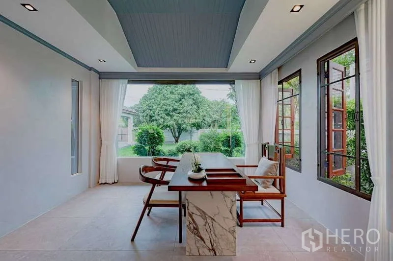 Detached House for rent or sale in Phra Khanong, Bangkok - Sunroom or study with large windows, marble-topped table, and views of the landscaped garden.