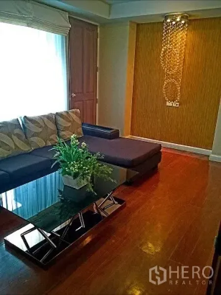 Condominium for rent in Pathum Wan, Bangkok - Cozy living room with an L-shaped sofa, glass coffee table, feature wall, and pendant light.