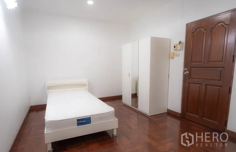 Townhouse for rent in Watthana, Bangkok - Simple bedroom with single bed, white wardrobe, and wooden door.