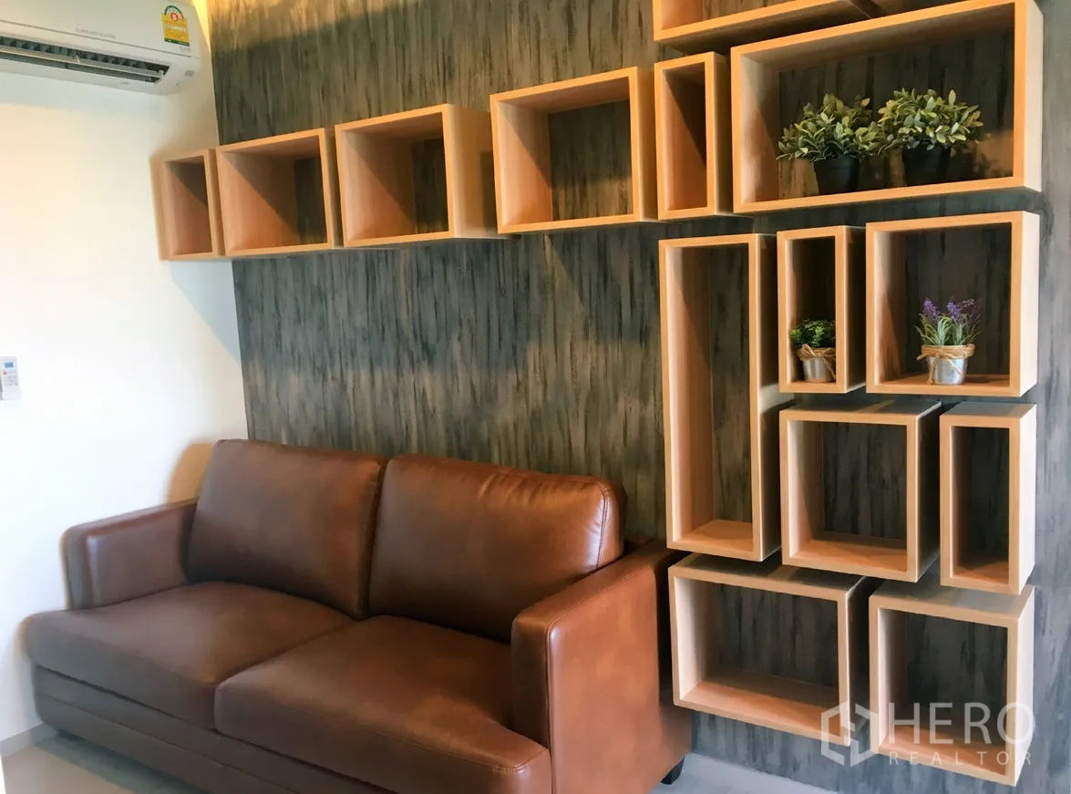 Condominium for rent in Khlong Toei, Bangkok - Living room with brown leather sofa and geometric wooden shelving with potted plants