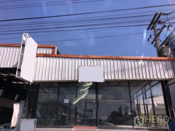 Retail Space for rent in Lam Luk Ka, Pathum Thani - Single-storey retail unit with floor-to-ceiling glass facade and corrugated metal awning on a roadside in Lam Luk Ka.