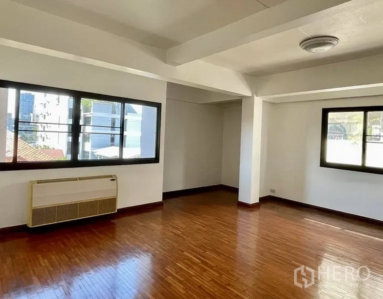 Home Office for rent in Khlong Toei, Bangkok - Corner room with large windows, polished wood floor and a wall-mounted air conditioner.
