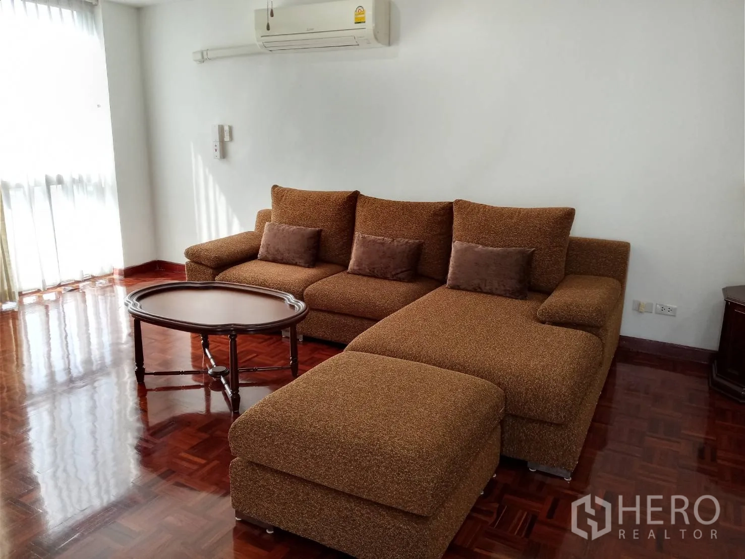 房间 出租在Watthana, Bangkok - 明亮客厅，棕色转角沙发、圆形茶几与抛光木地板。