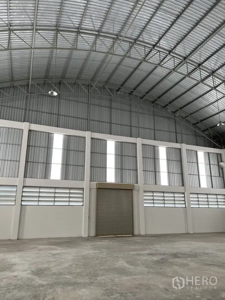 工厂 出租或出售在Bang Bo, Samut Prakan - 仓库墙面带多组采光板与中央卷帘门，屋顶挑高。