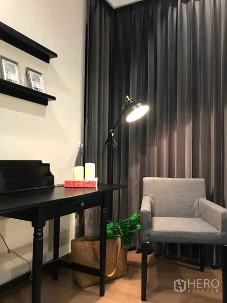 公寓 出租或出售在Ratchathewi, Bangkok - 工作角落配黑色书桌、灰色扶手椅、墙上置物架与落地窗帘。