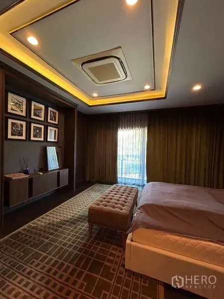 Detached House for rent in Bang Kapi, Bangkok - Spacious master bedroom with tray ceiling lighting, king bed, bench, floor-to-ceiling curtains, and built-in shelving.