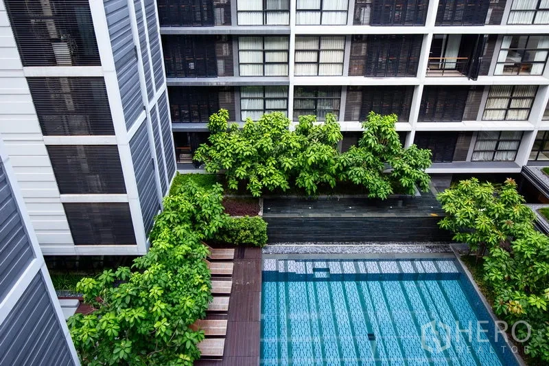 Condominium for rent in Watthana, Bangkok - Courtyard swimming pool surrounded by lush greenery and timber deck within a modern low-rise residence.