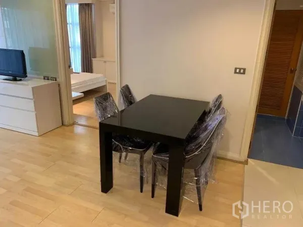 Condominium for rent in Pathum Wan, Bangkok - Open-plan living and dining area with a black table, TV console, light wood floors, and a sliding door to the bedroom.
