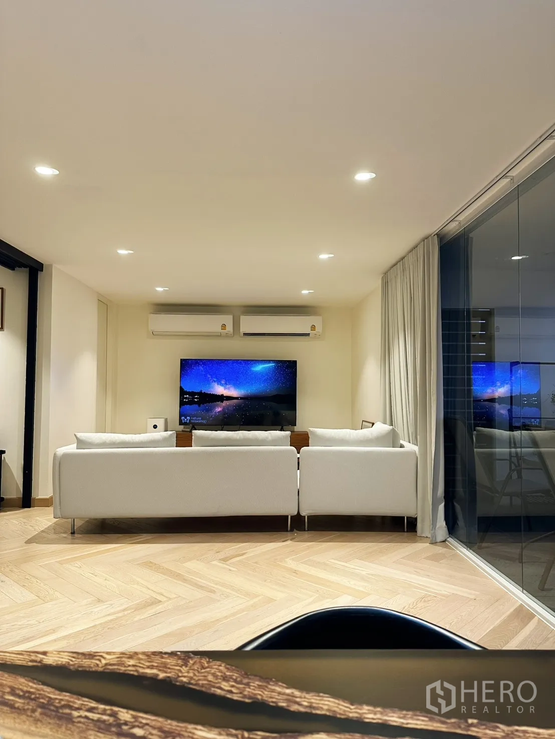 Condominium for rent or sale in Watthana, Bangkok - Cozy lounge setup with white sofa facing TV and balcony glazing.