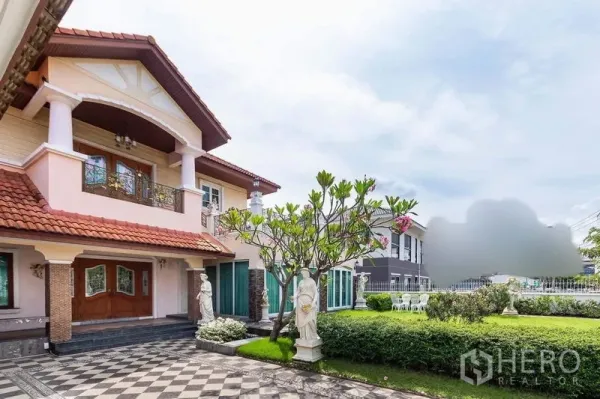 Detached House for rent or sale in Bang Khen, Bangkok - Grand entrance porch with double wooden doors, balcony columns, frangipani tree, and expansive front garden.