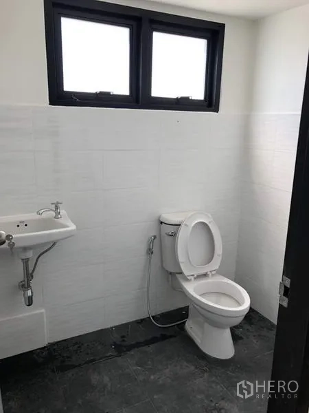 Factory for rent or sale in Lam Luk Ka, Pathum Thani - Clean restroom with white wall tiles, toilet, sink, and small ventilated windows.