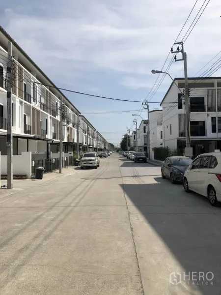 联排别墅 出租在Bang Kapi, Bangkok - 小区内部宽阔道路，两侧整齐的三层联排与路边停车。