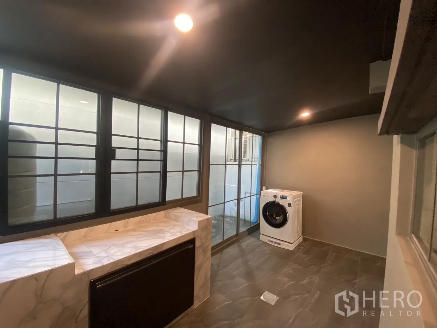 Townhouse for rent in Bang Kapi, Bangkok - Utility room with large windows, marble countertop and front-loading washing machine.