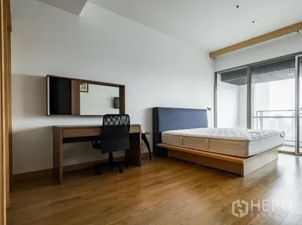 公寓 出租在Watthana, Bangkok - 宽敞主卧，平台床与书桌，可直通阳台俯瞰城市天际线。