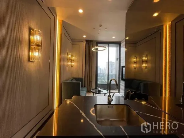 Condominium for rent in Khlong Toei, Bangkok - Open‑plan living room viewed from a black marble kitchen island, with ring pendant lighting and floor‑to‑ceiling window to a city‑view balcony.