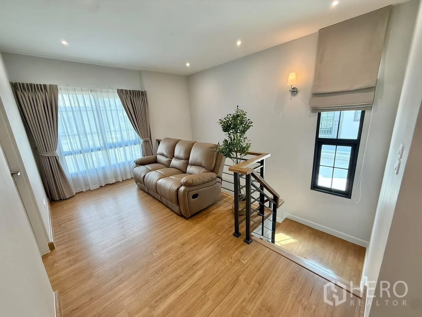 Detached House for rent in Bang Phli, Samut Prakan - Upstairs family lounge with leather sofa beside the stair landing, wood floors and full-height drapes.