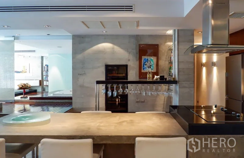 Condominium for rent or sale in Khlong Toei, Bangkok - Modern kitchen with island cooktop, stainless appliances and hanging wine glasses facing a spa area.