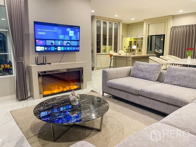 Detached House for rent in Bang Khen, Bangkok - Modern living room with grey sofa, marble coffee table, wall-mounted TV and electric fireplace.