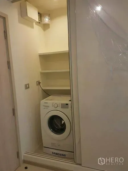 Condominium for rent in Khlong Toei, Bangkok - In-unit laundry closet with front-loading washing machine and built-in shelves.