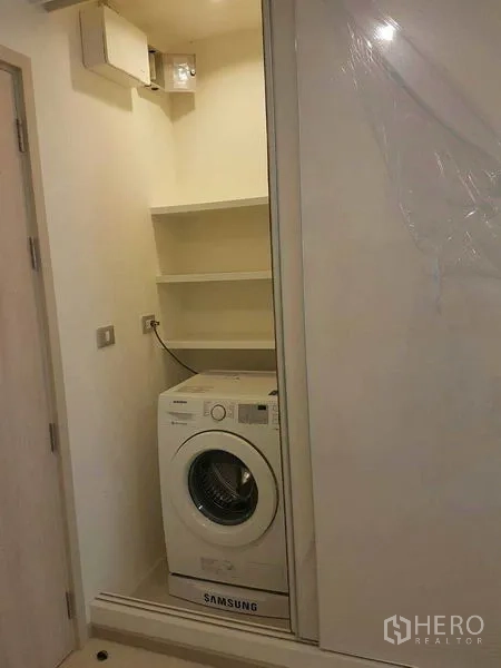 Condominium for rent in Khlong Toei, Bangkok - In-unit laundry closet with front-loading washing machine and built-in shelves.