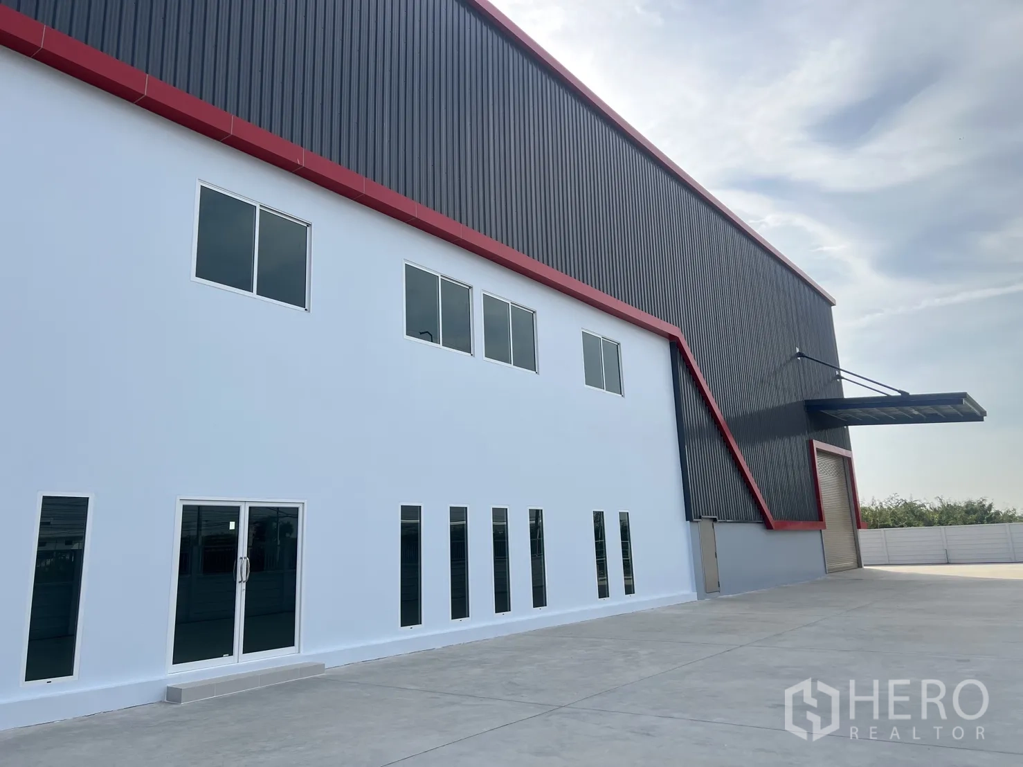 Warehouse for rent in Mueang Samut Prakan, Samut Prakan - Close-up of the white two-storey office facade beside the warehouse with a wide driveway and loading canopy.