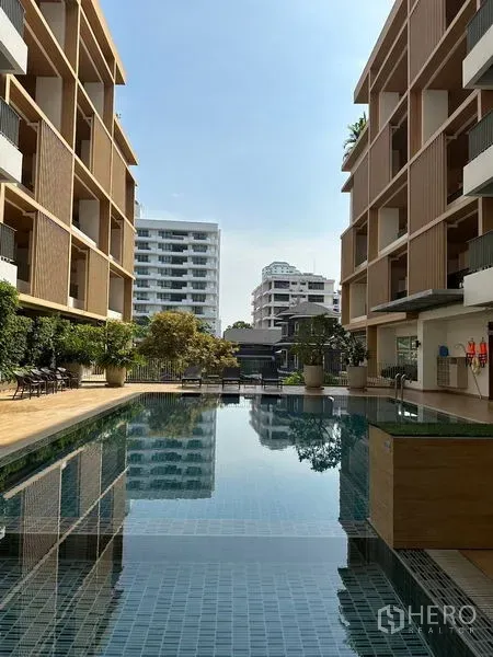 Apartment for rent in Khlong Toei, Bangkok - Outdoor lap pool between modern low-rise buildings with sun loungers.